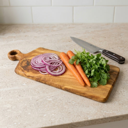 Olive wood chopping board with ring handle on a kitchen worktop with red onion, carrots and herbs