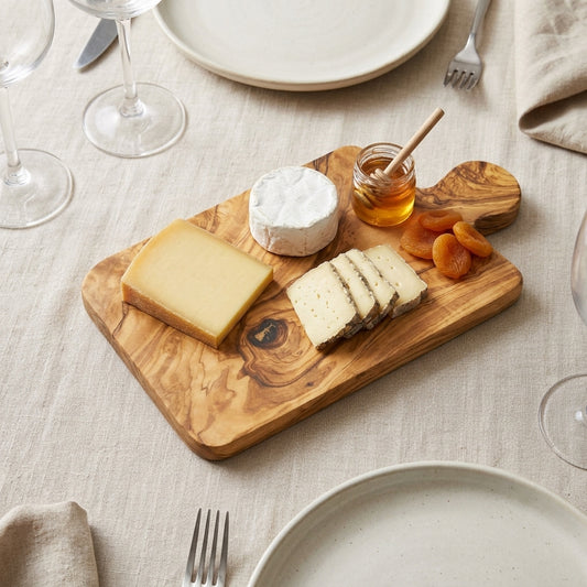 Olive wood cheese platter with cheeses, honey and dried apricots on a laid linen table