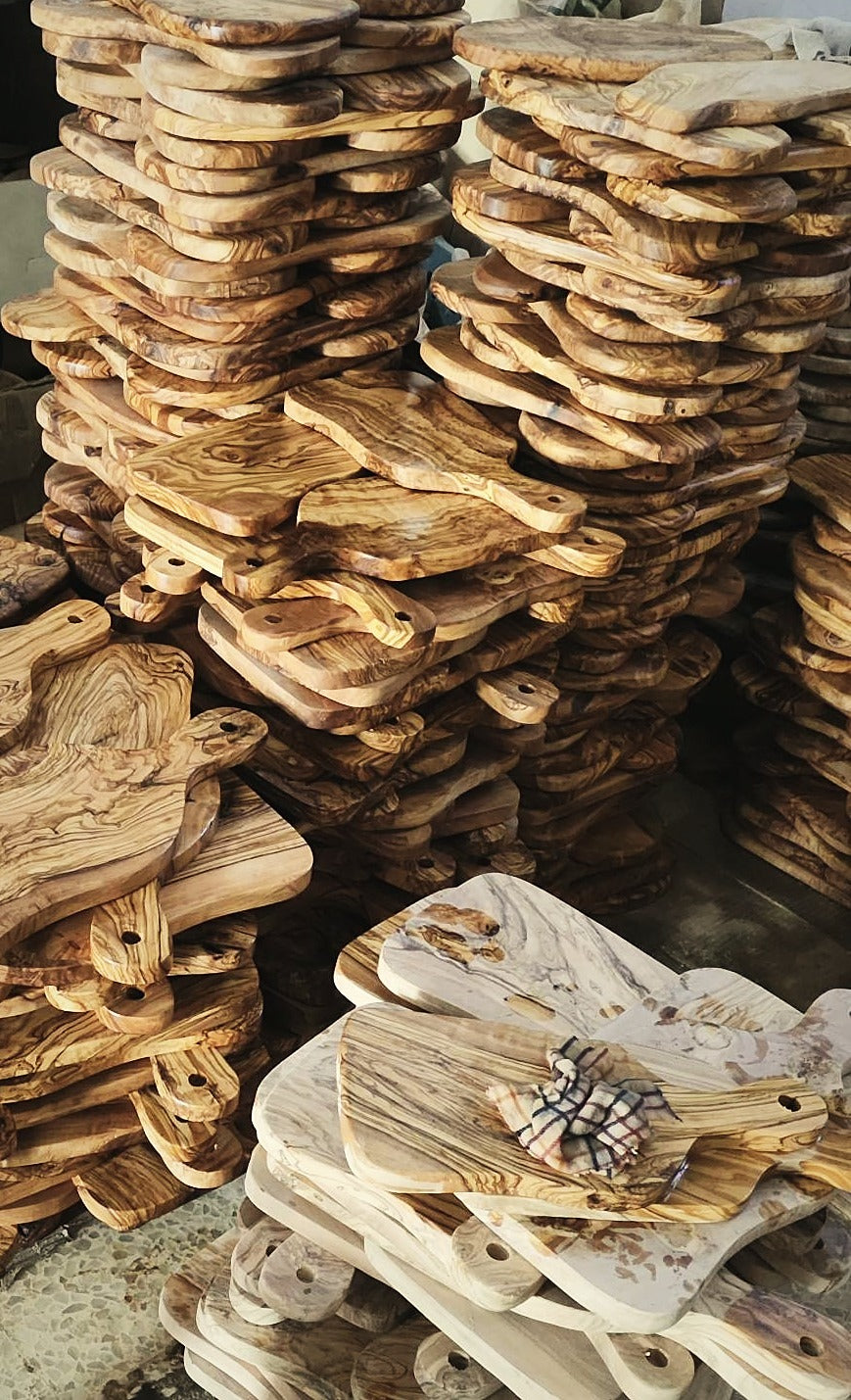 Stacks of handmade olive wood cutting boards in the workshop