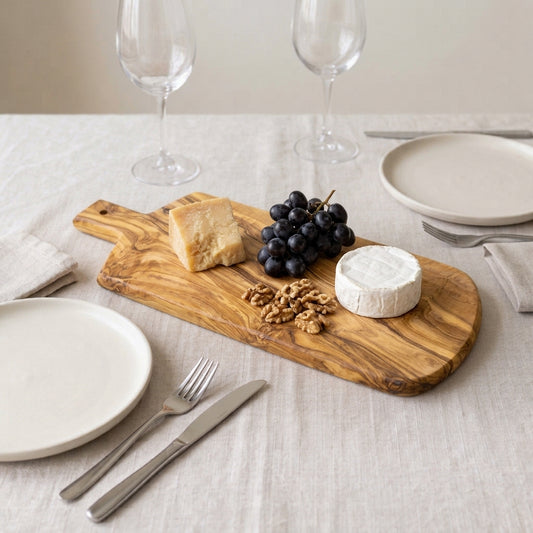 Shield-shaped olive wood serving board on a set table, with cheeses, grapes and walnuts