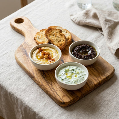 Olive wood paddle board with toasted bread, hummus and dips on a linen tablecloth